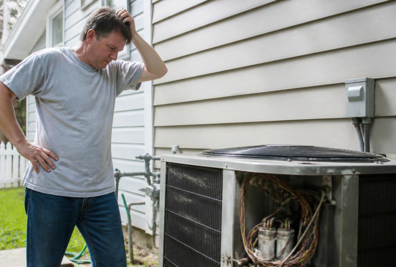 Homeowner inspecting a broken outdoor air conditioning unit
